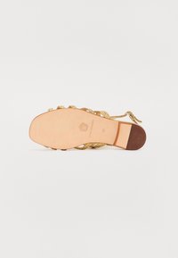 Gullfarget flettet sandal med stropp, nude lærsåle og lav, rektangulær hæl; har en sikret ankelrem og subtilt logoimprint.