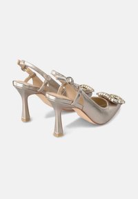 Talons slingback dorés métalliques avec des embellissements en bijoux proéminents, un bout pointu, et une sangle de cheville texturée. Talon de forme carrée.