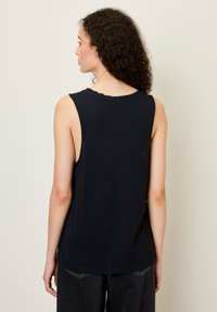 Jūros mėlynos spalvos be rankovių palaidinė su banguoto krašto iškirpte ir atsipalaidavusiu siluetu. Minkšta medžiaga, minimalus dizainas ir šiek tiek ilgesnė nugaros dalis.