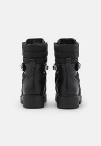 Botas negras hasta el tobillo con parte superior de tejido acolchado, puntera redonda y suela gruesa. Presenta acentos decorativos en los lados y tiradores para facilitar el uso.