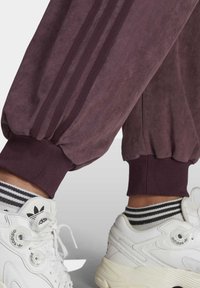 Bordeaux joggers med ribbade muddar och tre mörkare ränder längs hela benet. Matchade med vita sneakers och svart-vita randiga strumpor.