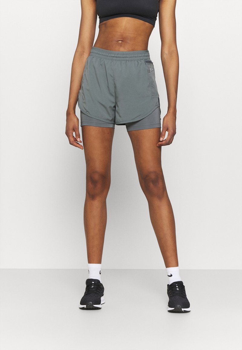 Shorts deportivos grises con una cintura elástica y bolsillos laterales, confeccionados en un material ligero y con un corte holgado, combinados con zapatillas negras.
