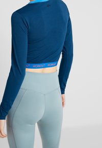Navy long-sleeve workout top with a cropped design and pink "WORKOUT" band. Paired with light gray high-waisted leggings featuring textured accents.