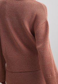 Stickad tröja i rostfärg, med ribbat nederkant och ärmslut, lös passform och texturerad tyg som har en subtil glans.