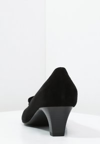 Escarpin en daim noir avec un bout pointu, un talon bloc de hauteur moyenne, une texture lisse, un design minimaliste et sans embellissements visibles.
