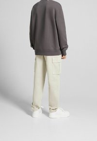 Grå sweatshirt med avslappnad passform, matchad med beige cargobyxor med sidofickor och vita sneakers. Enkel design med minimala detaljer.