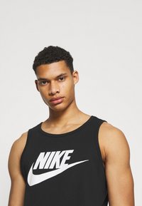Sort Nike tank top har et stort hvidt logo på forsiden. Stoffet ser blødt ud med et klassisk ærmeløst design.