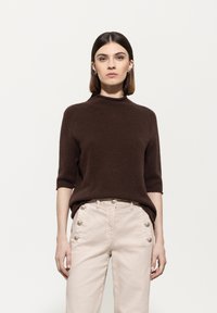 Brown short-sleeve sweater with a high neck. Paired with light-colored pants featuring button accents on the sides. Smooth texture.