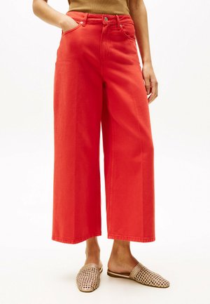 Jeans anchos rojos de mezclilla 100% algodón con cintura alta, dos bolsillos frontales y detalles de costura sutiles. Combinados con zapatos de lona tipo slip-on.