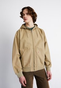 Bežna zip-up kapuca z vrvico na kapuci, veliki sprednji žepi, rebrasti manšeti in majhen logotip na levi strani.