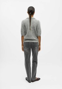 Grauer Strickpullover mit Kragen, kurz puffy Ärmeln, kombiniert mit grauen geraden Jeans. Model trägt dunkle Ballerinas und wird von hinten betrachtet.