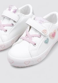 Zapatillas sintéticas blancas con una textura suave, detalles en forma de corazón en rosa y azul, y cordones elásticos combinados con una correa de Velcro.