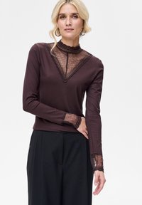 Brązowa bluzka z długim rękawem, z koronkową wstawką i wysokim kołnierzem oraz koronkowymi akcentami na mankietach. Miękki materiał o gładkiej fakturze.