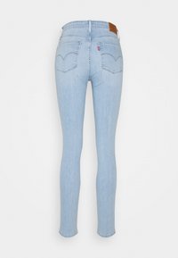 Jeans ajustados de mezclilla azul claro, con una cintura alta, bolsillos traseros con detalles de costura y una etiqueta de piel marrón en la parte posterior.