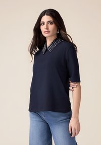 Haut navy à manches courtes avec un col texturé orné de clous en métal. Tissu doux et lisse avec une coupe décontractée.