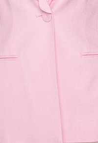 Giacca rosa chiaro realizzata in tessuto testurizzato, con colletto rotondo, chiusura a singolo bottone e due tasche anteriori con cuciture decorative.