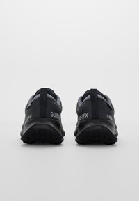 Black waterproof shoes with Gore-Tex branding, featuring a textured outsole, padded collar, and contrasting gray inner lining.