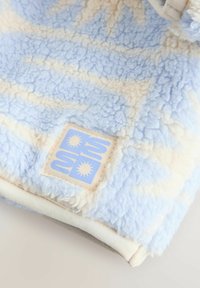 Soft fleece fabric in light blue and cream with a sewn square patch featuring a stylized sun design in light blue and cream.