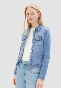Chaqueta de mezclilla azul claro con botón frontal, dos bolsillos en el pecho y un cuello clásico. Suave textura y diseño entallado realzan su forma.