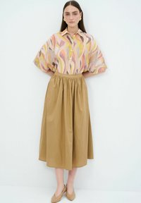Camicia a maniche corte con bottoni color rosa e beige con motivi ondulati, abbinata a una gonna lunga e arricciata color sabbia. Completata da dei ballerine beige.