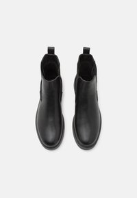 Bottines en cuir noir avec une finition lisse, des panneaux latéraux élastiques et des tirettes pour un enfilage facile ; semelles en caoutchouc robustes.