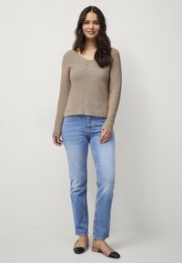 Beige geribd sweater met een V-hals, gecombineerd met lichtblauwe rechttoe-rechtaan jeans en zwarte ballerina's, met een subtiel two-tone ontwerp.