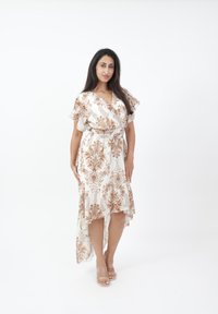 Hvid kjole med brunt blomsterprint, flæse shorts ærmer, snøret talje og høj-lav kant. Glat stof og transparente sandaler.