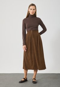 Ruda, klostuota kordurojo sijonas su aukštu liemeniu ir mygtukų detalėmis, derinamas su prigludusia rudą turtleneck ir juodais plokščiais bateliais.