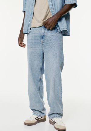 Lysblå denimjeans med en afslappet pasform, der har et klassisk fem-lomme-design og detaljer med stikninger. Bæres med hvide og beige sneakers.