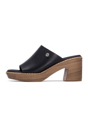 Mule abierto de cuero negro con tacón grueso imitación madera y detalle de costuras blancas, con un pequeño detalle metálico del logo en la parte superior.