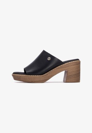 Mule abierto de cuero negro con tacón grueso imitación madera y detalle de costuras blancas, con un pequeño detalle metálico del logo en la parte superior.