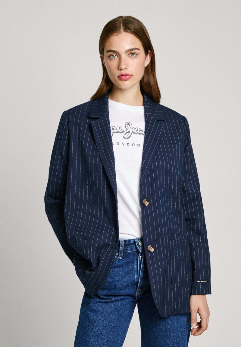 Blazer de rayas marinas con solapa con muesca, dos botones y tejido texturizado, llevado sobre una camiseta gráfica blanca y jeans azules.