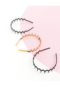 Drie haarbanden: zwart en oranje, met zigzagpatronen en gestructureerde oppervlakken. Elke band heeft een flexibele structuur en is geplaatst op een roze achtergrond.