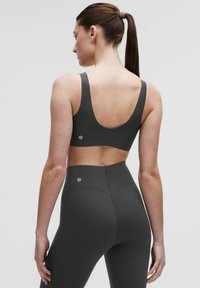 Pelēks sporta krūšturis un augsta jostasvieta legingi, kas izgatavoti no elastīga materiāla. Krūšturim ir zems aizmugure un platas siksnas; abiem ir logo detaļas.