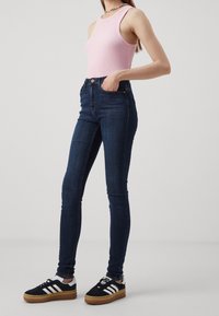 Rosa ribbat tanktop kombinerad med högmidjade mörkblå skinny jeans och svarta sneakers med vita ränder och en gummisula.