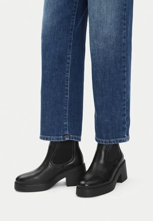 Stivaletti con plateau in pelle nera indossati con jeans blu a gamba dritta su sfondo semplice.