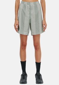 Ljust gröna shorts med ett geometriskt mönster, elastisk midja och sidofickor, nedstoppade med svarta strumpor och mörka skor.