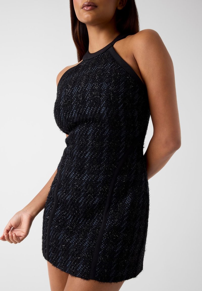Schwarzes Tweedkleid mit strukturierter Oberfläche, Neckholder-Ausschnitt und kontrastierendem schwarzen Besatz. Figurbetonte Form mit vertikalen Nähten.