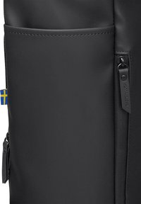 Black backpack featuring a smooth, matte texture, zipper pocket on the side, and a blue and yellow accent tab. Minimalist design with clean lines.