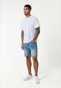 T-shirt de algodão branco, calções de ganga azuis e ténis brancos. Design simples, mangas curtas e corte descontraído.