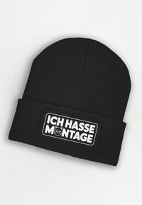 Black knit beanie featuring a rectangular patch with the text "ICH HASSE MONTAGE" and a cat graphic in white. Ribbed texture throughout.