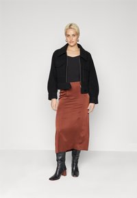 Svart cropped jakke med to store frontlommer, brukt over en svart topp og et rustfarget satin midi skjørt. Svart hælboots fullfører antrekket.