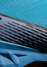 Tige de chaussure de sport bleue en tissu texturé, au design superposé, avec une semelle en caoutchouc dotée d'un motif texturé pour une meilleure adhérence.