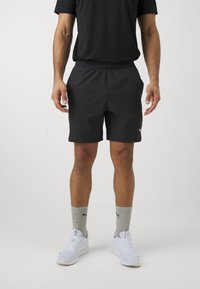 Svarte treningsshorts med elastisk midje, kombinert med grå sokker med logo, og hvite joggesko. Enkelt, lett design.