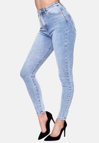 Jeans de tiro alto en lavado claro con un ajuste slim, que presentan una textura suave y un ligero desgaste, combinados con zapatos de tacón alto negros.