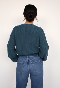 Miętowy sweter dziergany o prążkowanej fakturze z opuszczonymi ramionami, w połączeniu z wysokim stanem niebieskich dżinsów o klasycznym kroju z pięcioma kieszeniami.