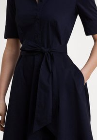 Tmavomodré šatové šaty z hladkej látky, s krátkymi rukávmi, zaväzovaným pásom a bočnými vreckami s voľne padajúcou sukňou.