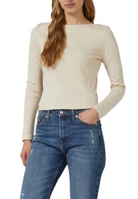 Beżowa bluzka z długim rękawem z dekoltem typu łódka i zdobieniami na ramionach, zestawiona z wyblakłymi niebieskimi jeansami z przetarciami o klasycznym kroju.
