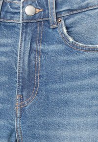 Blå denimjeans med en klassisk femficksdesign, kontrasterande sömmar, en metallknappsstängning och slitna detaljer vid fickan.