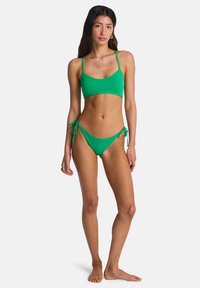 Σετ μπικίνι φωτεινού πράσινου χρώματος με επενδυμένο τοπ που διαθέτει λεπτές τιράντες και κάτω μέρος χαμηλής μέσης με δεσίματα στο πλάι. Ομαλό ύφασμα και μινιμαλιστικός σχεδιασμός.